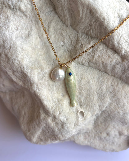 Silhouette Spark CLOE necklace 近距離特寫，金色鍊條搭配白色陶瓷魚吊墜與藍眼珍珠圓珠，石材紋理背景
