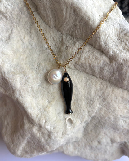 Silhouette Spark NICO necklace 近距離特寫，黑色陶瓷魚吊墜與珍珠圓珠，石材紋理背景