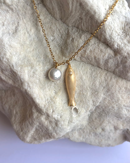 Silhouette Spark THEA necklace 近距離特寫，金色魚形吊墜與珍珠圓珠，石材紋理背景